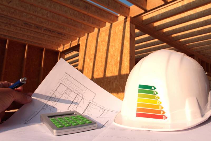 Casque de chantier avec étiquette d'efficacité énergétique et plans de construction sur un chantier immobilier.